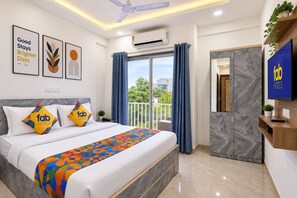 A hotel room with a bed, a TV, a balcony with curtains, and a wall-mounted air conditioner.