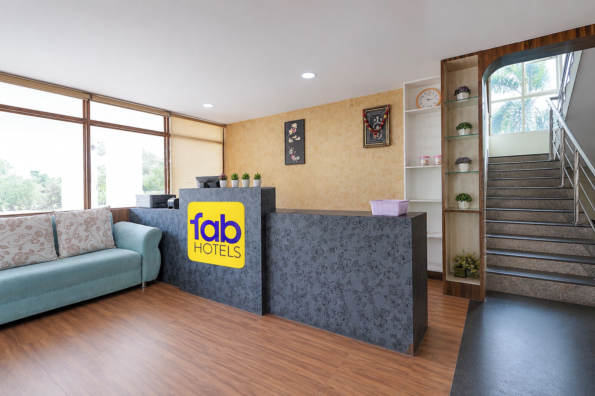 A hotel reception area with a sofa, a reception desk, a staircase, and a wall with framed pictures.