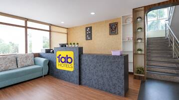 A hotel reception area with a sofa, a reception desk, a staircase, and a wall with framed pictures.