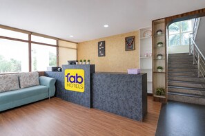 Zona de recepción de un hotel con un sofá, un mostrador de recepción, una escalera y una pared con cuadros enmarcados.