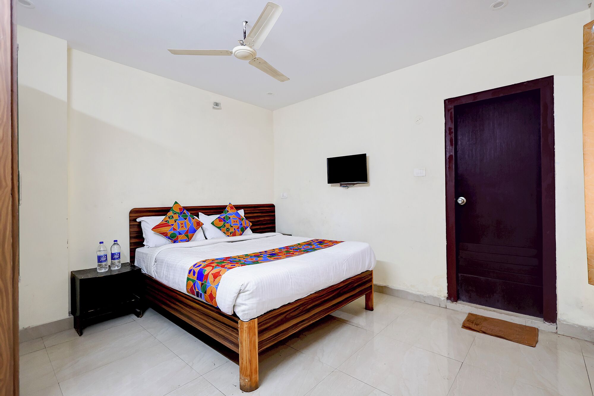 A hotel room with a bed, a television, a ceiling fan, and a wooden door.