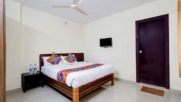 A hotel room with a bed, a television, a ceiling fan, and a wooden door.