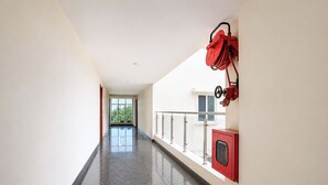 Un pasillo con una puerta de cristal que da a un balcón, un extintor rojo montado en la pared y un armario rojo.