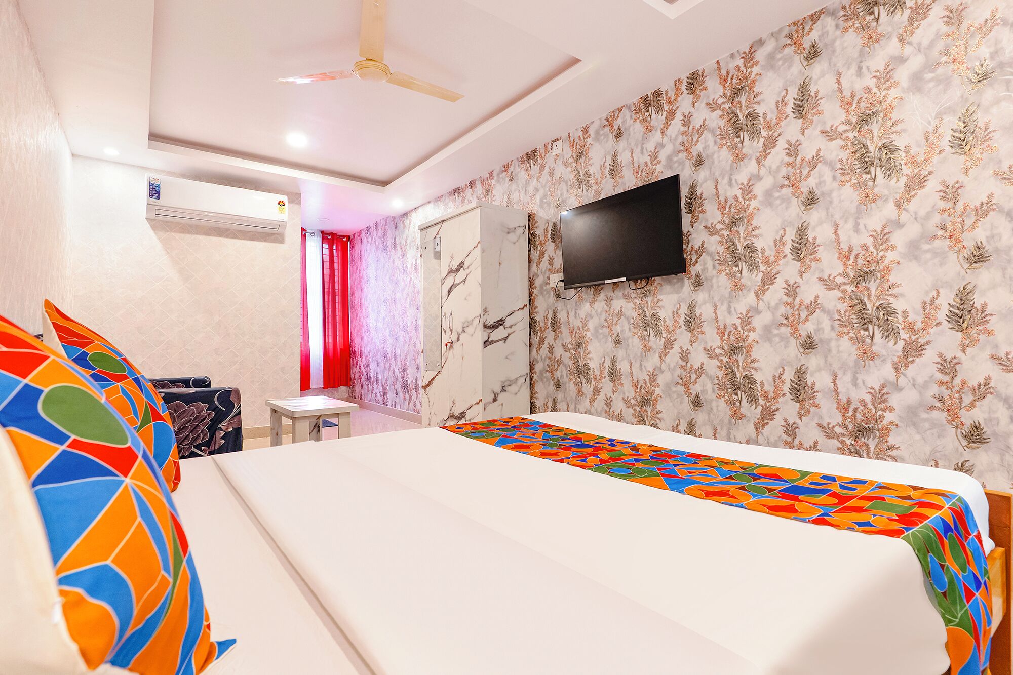 Quarto de hotel com cama, televisão na parede, ventoinha no teto e banheiro com cortina de chuveiro.