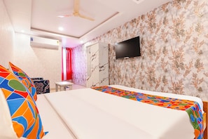 A hotel room with a bed, a television mounted on the wall, a ceiling fan, and a bathroom with a shower curtain. - FabHotel Sj Comforts (Bangalore)