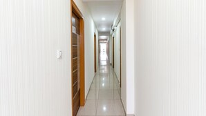 A corridor with doors on both sides, a tiled floor, and a ceiling with recessed lighting. - Fabhotel Sj Comforts (Bangalore)