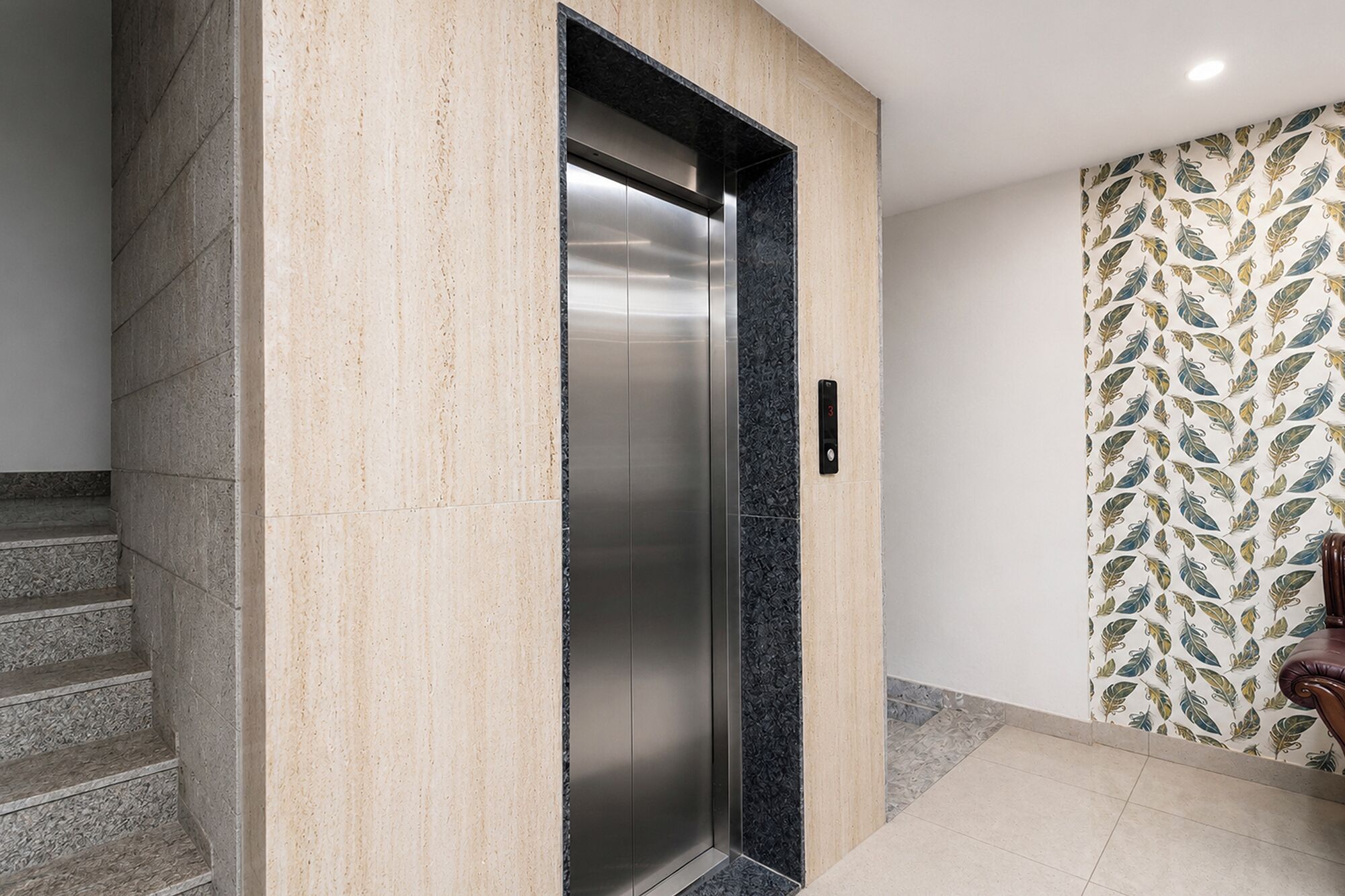 A modern elevator with a metallic finish, adjacent to a staircase and a patterned wall.