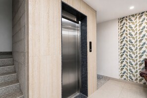 Un ascensor moderno con acabado metálico, junto a una escalera y una pared con diseño.