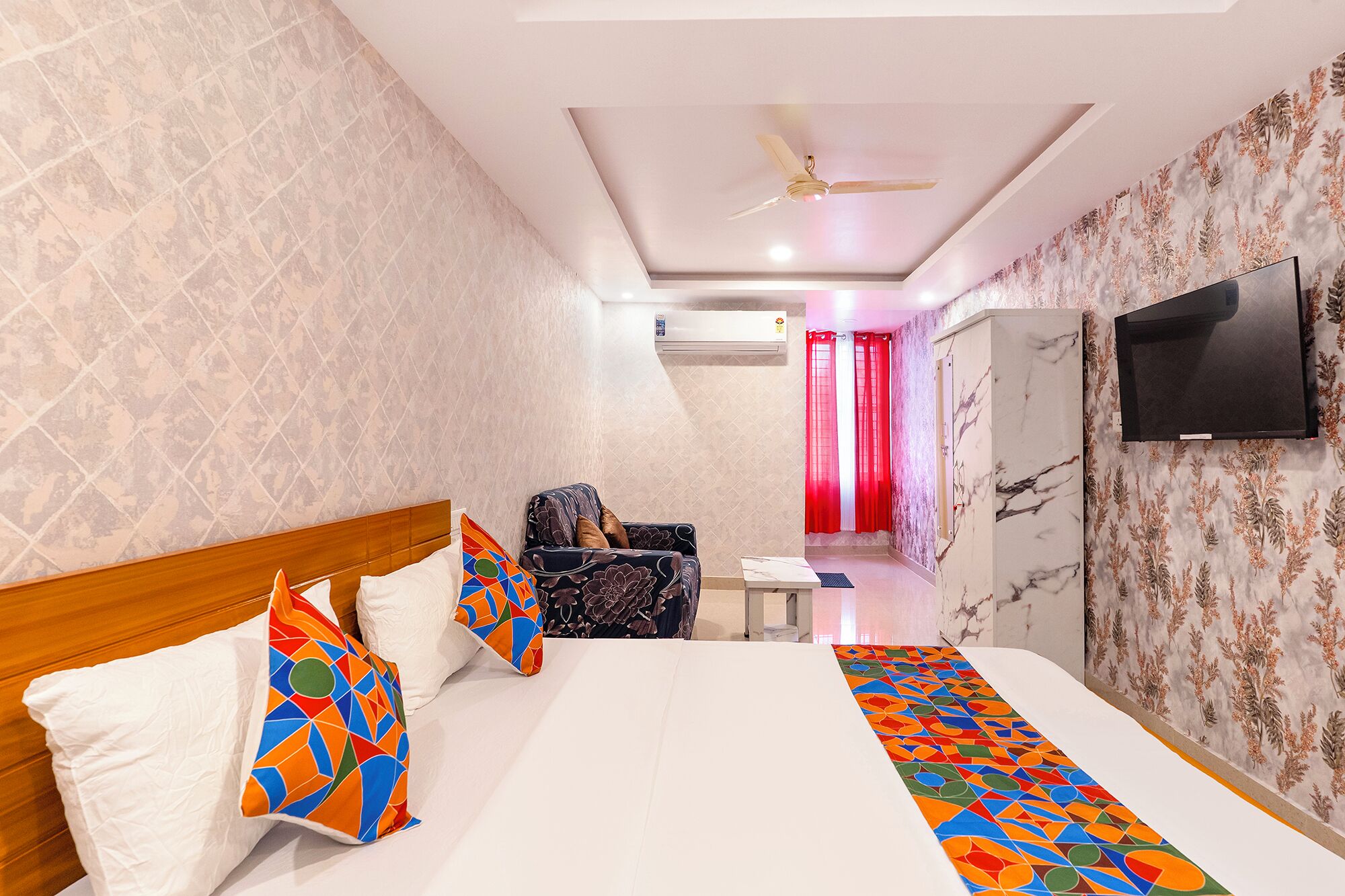 A hotel room with a bed, a chair, a TV, and a ceiling fan.