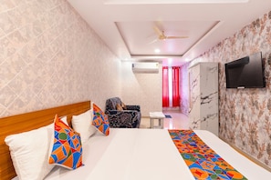 Habitación de hotel con cama, una silla, un televisor y un ventilador de techo.