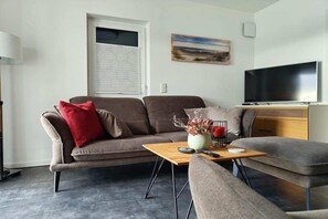 A modern living room with a sofa, a coffee table, a TV, and a painting on the wall. - Modernes Apartment mit Blick auf den Hafen in Rechlin (Rechlin)