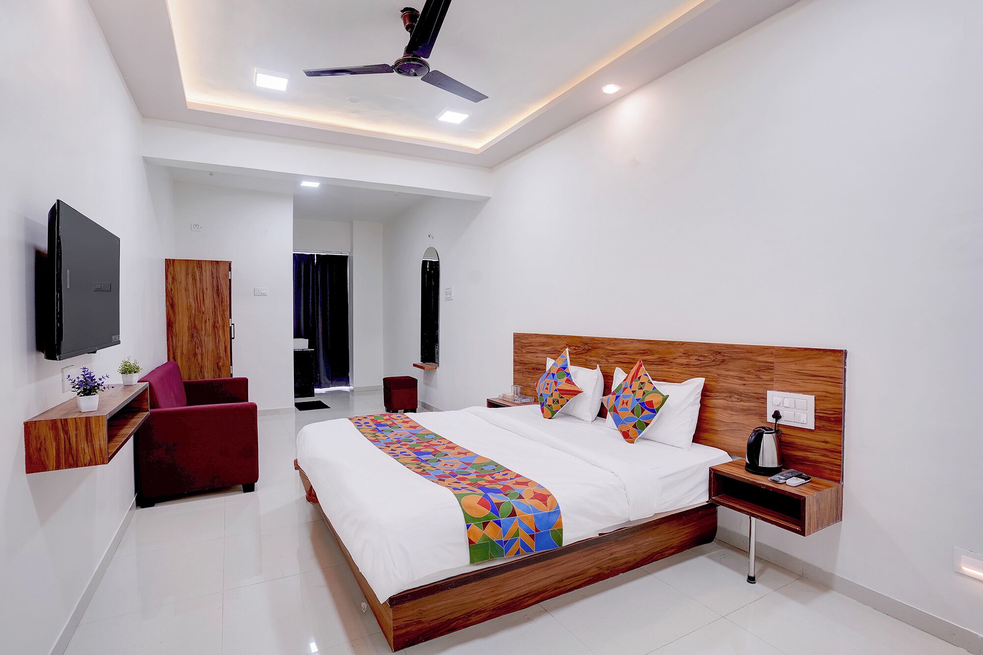 A modern hotel room with a large bed, a flat-screen TV, a wooden headboard, and a ceiling fan.
