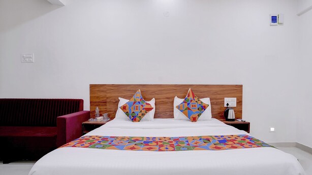 A hotel room with a large bed, a wooden headboard, a red armchair, a bedside table with a lamp, and a small wall clock. - FabHotel Nashik Prime Stay (Nashik)