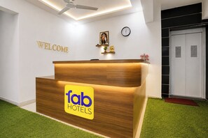 Una recepción con detalles de madera y el logotipo de 'fab hotels'. Un cartel con la palabra 'BIENVENIDOS' sobre el mostrador y un reloj en la pared.