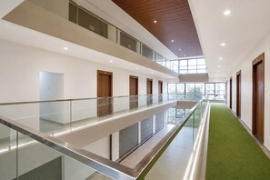 Un interior moderno con barandilla de vidrio, un pasillo alfombrado de color verde y puertas de madera.