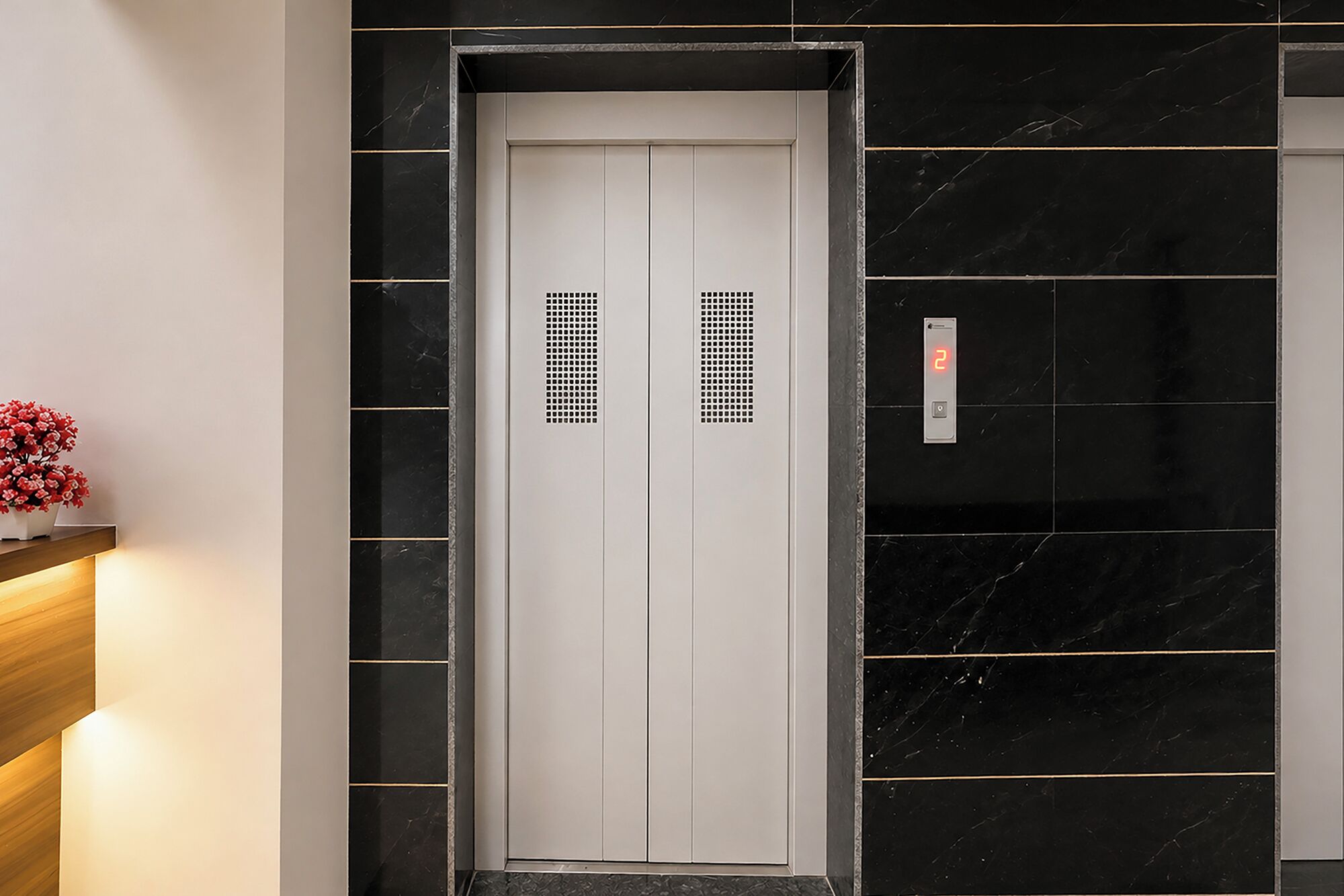 En elevator med et digitalt display, der viser nummer 2, omgivet af sorte marmorvægge med guldlinjer.