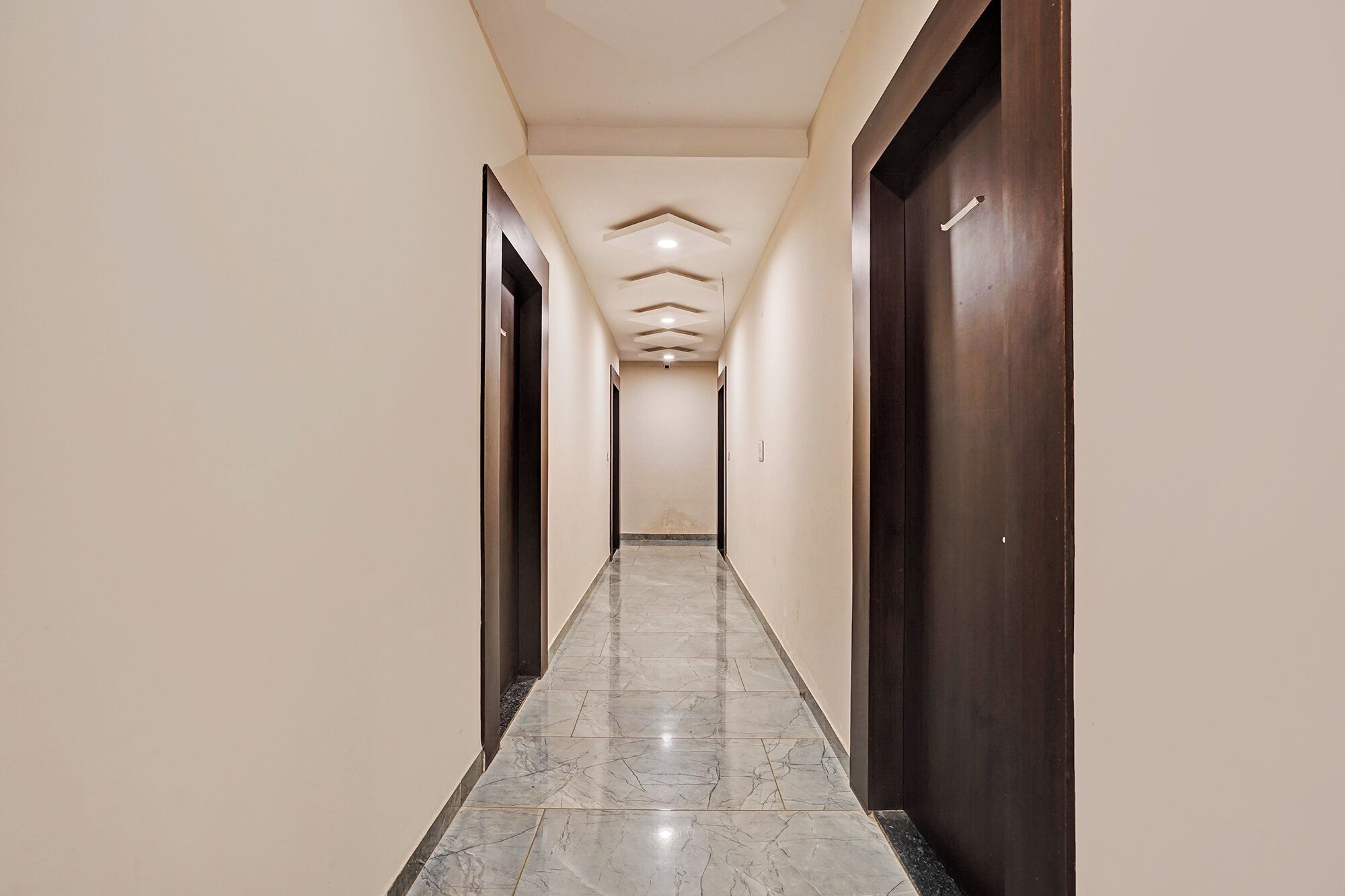 A corridor with a marble floor, wooden doors, and a ceiling with recessed lighting.