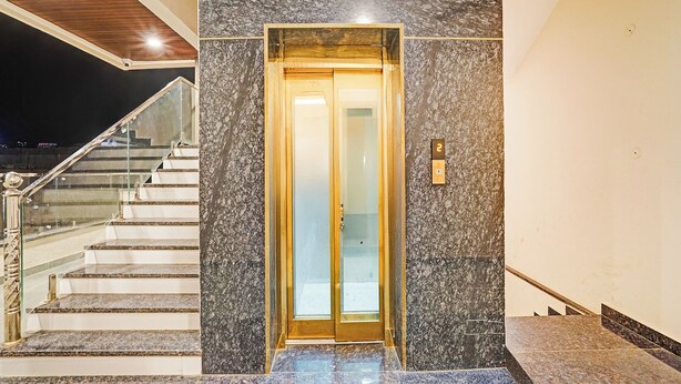 Een moderne gevel met glazen lift, marmeren trappen en een metalen leuning.