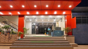 Een hotelgevel in het rood, met een trap die naar de ingang leidt en plantenbakken bij de voet.
