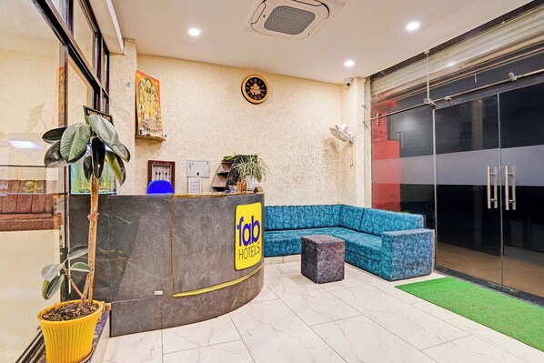 A hotel reception area with a curved counter, a blue sofa, and a potted plant. - Fabhotel Shivlok (Bhopal)