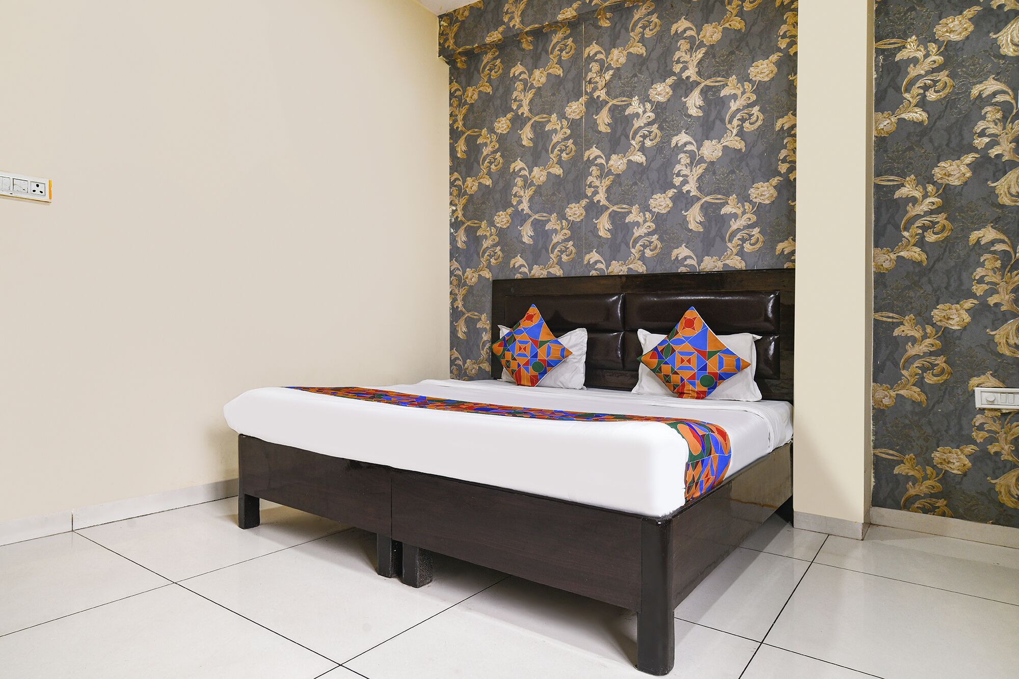 Una cama con cabecera oscura, ropa de cama blanca y almohadas geométricas coloridas.