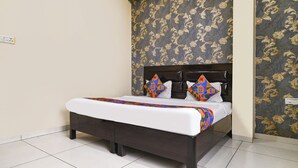 Una cama con cabecera oscura, ropa de cama blanca y almohadas geométricas coloridas.