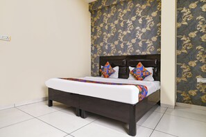 Una cama con cabecera oscura, ropa de cama blanca y almohadas geométricas coloridas.