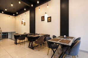 A dining area with tables and chairs, overhead lighting, and framed signs on the walls. - FabHotel Shree I (Indore)