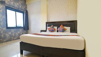 A hotel room with a large bed, a window, and patterned wallpaper.