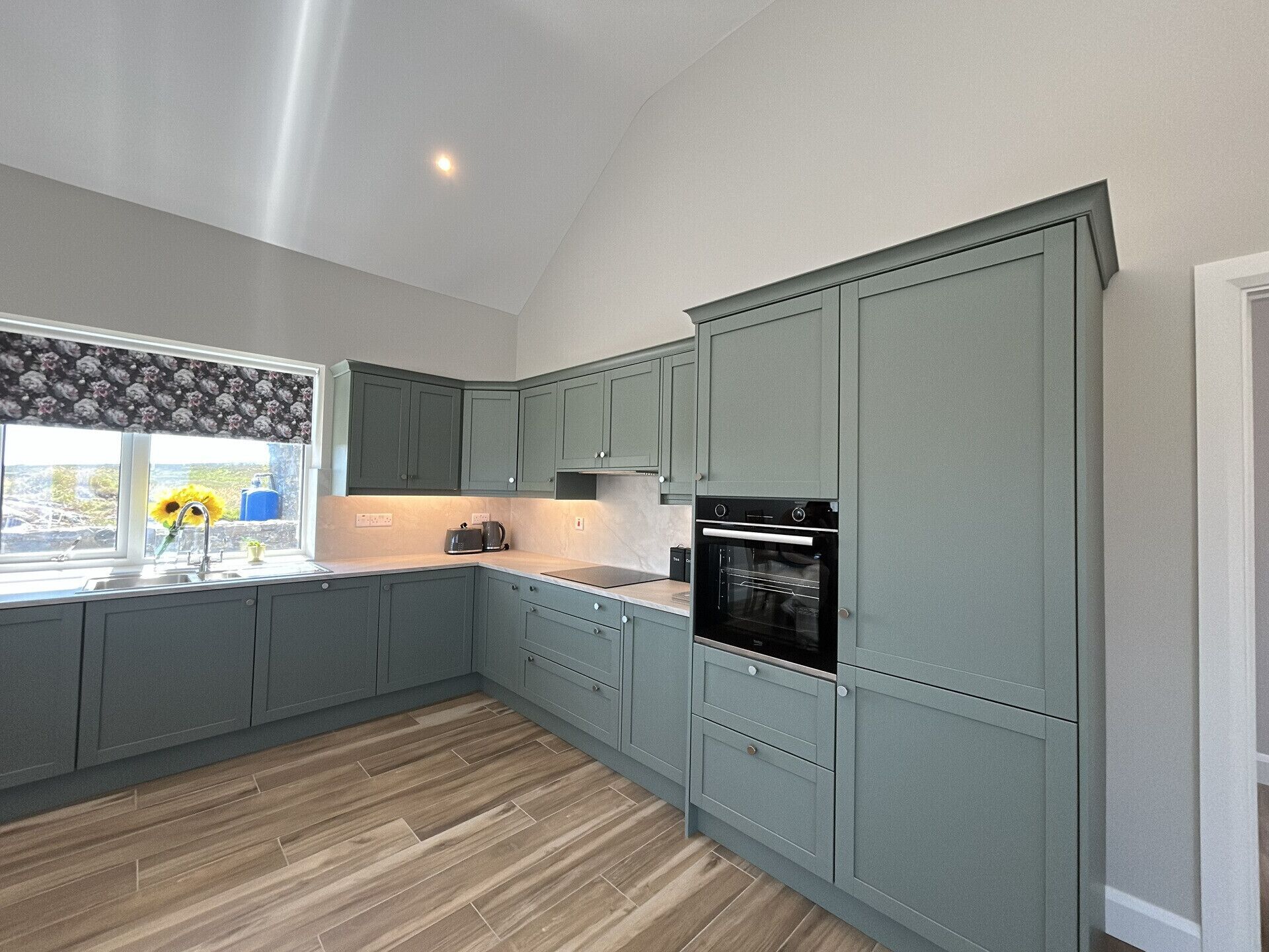 A modern kitchen with grey cabinets, a black oven, and a window with a floral curtain.
