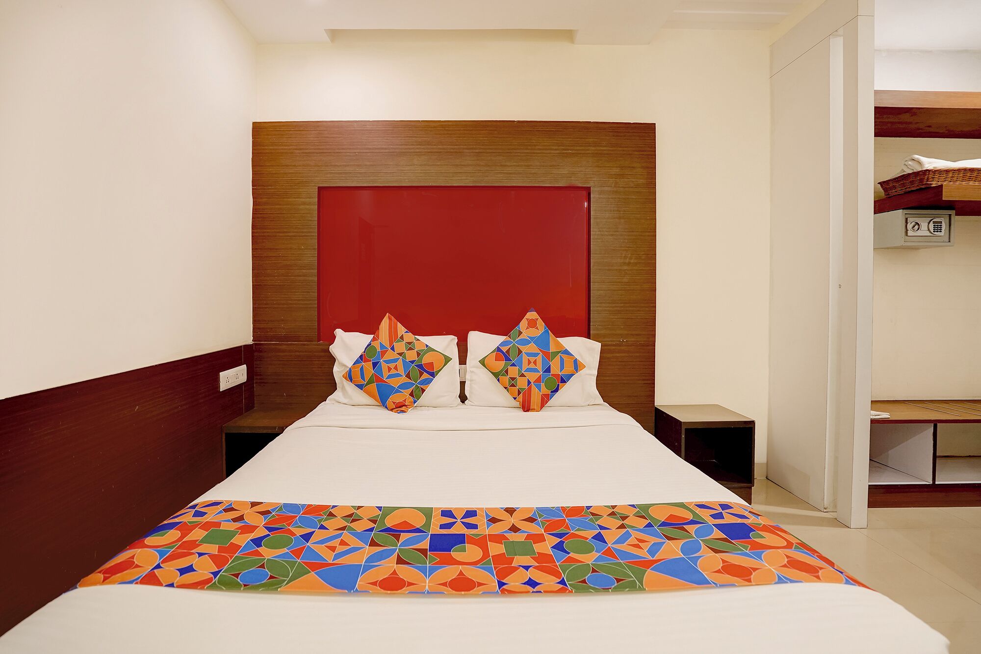 A hotel room with a large bed, two pillows with geometric patterns, a wooden headboard, and a bedside table.