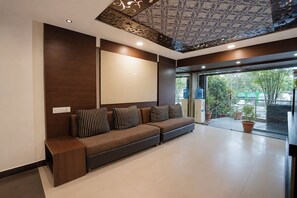 A modern waiting area with a sofa, a flat-screen TV, and a view of the outdoors. - FabHotel Gn International (Hyderabad)