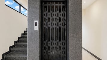 Una entrada moderna con una reja de metal negro, una escalera con escalones negros y una pared texturizada.