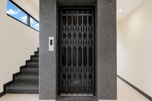 A modern entrance with a black metal gate, a staircase with black steps, and a textured wall.