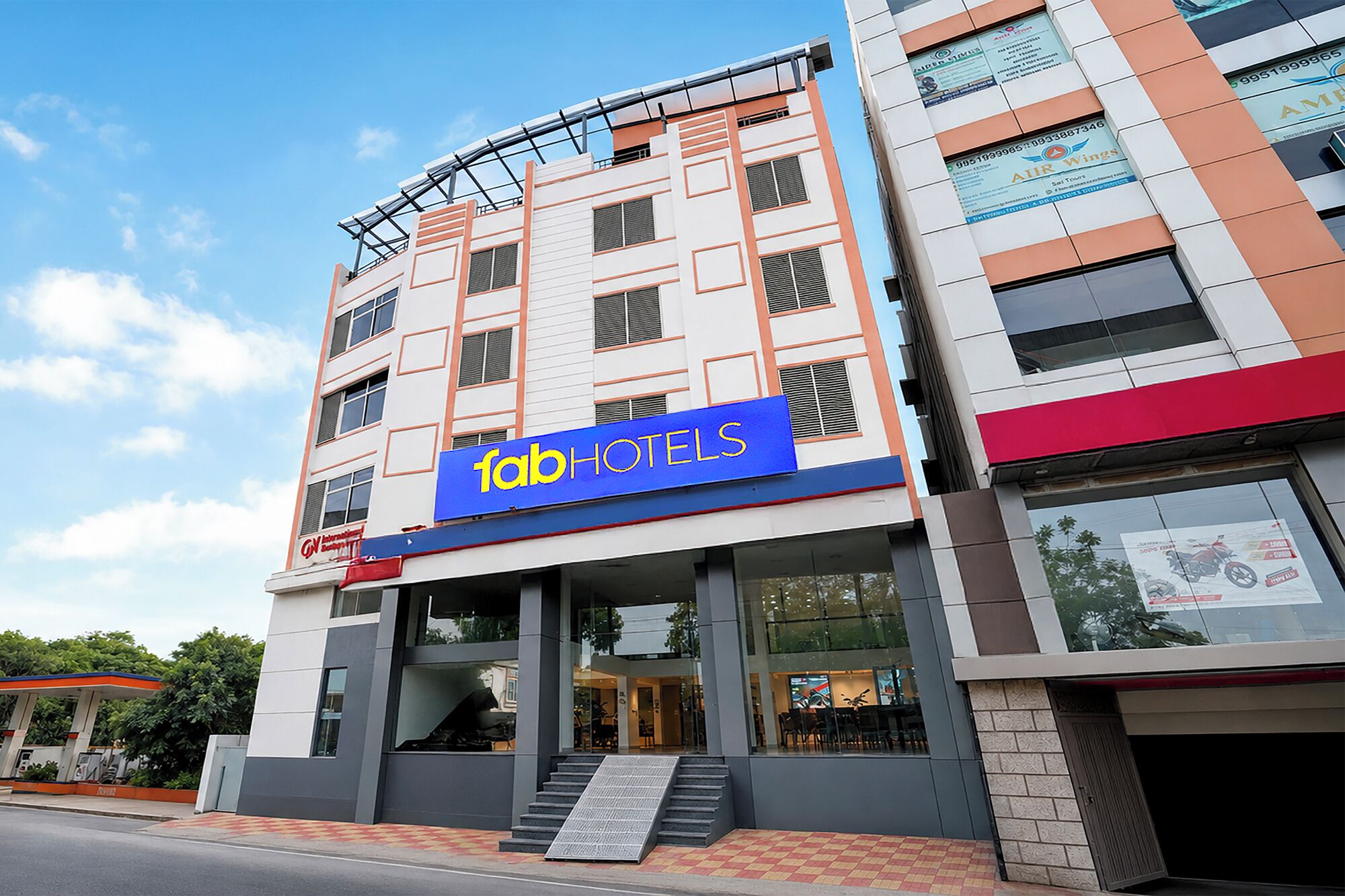 Um hotel com vários andares e um destaque para a placa 'fab hotels', uma entrada visível e uma escadaria que leva à entrada.