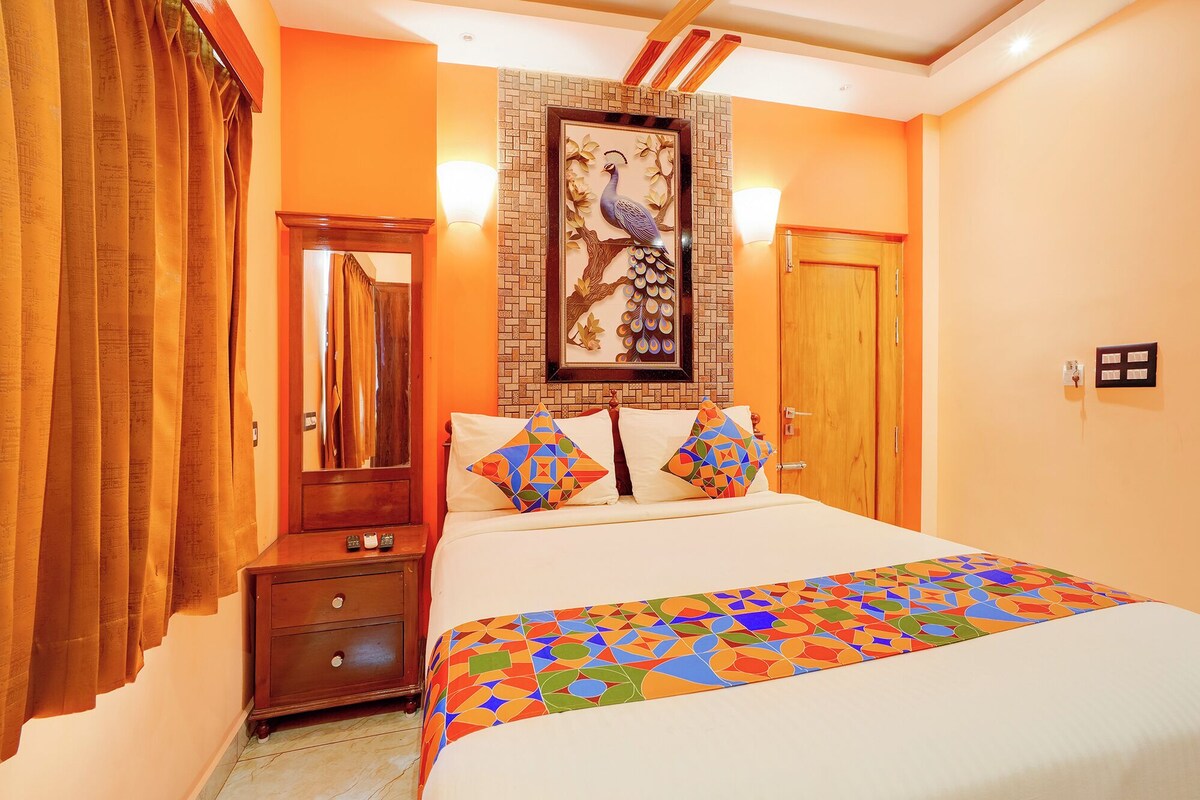 Una habitación de hotel con cama, mesita de noche, espejo, lámpara de pared y puerta.