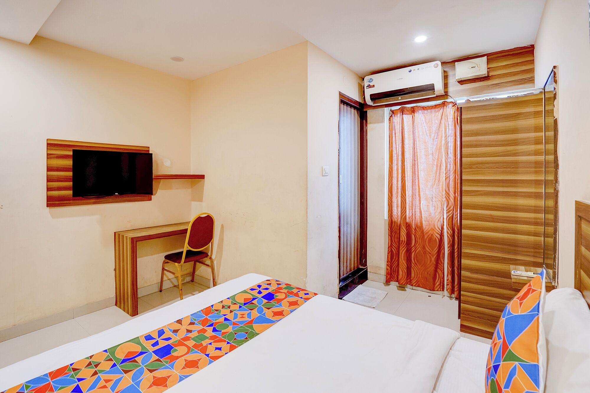 Habitación de hotel con cama, escritorio con silla, televisor, equipo de aire acondicionado y ventana con cortinas.