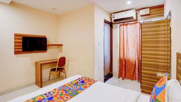 Habitación de hotel con cama, escritorio con silla, televisor, equipo de aire acondicionado y ventana con cortinas.