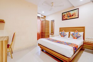 A hotel room with a large bed, a wooden headboard, a painting on the wall, and a ceiling fan.