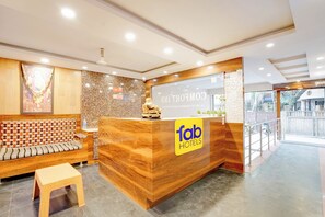 A hotel reception area with a wooden reception desk, a seating area with patterned cushions, and a decorative wall.