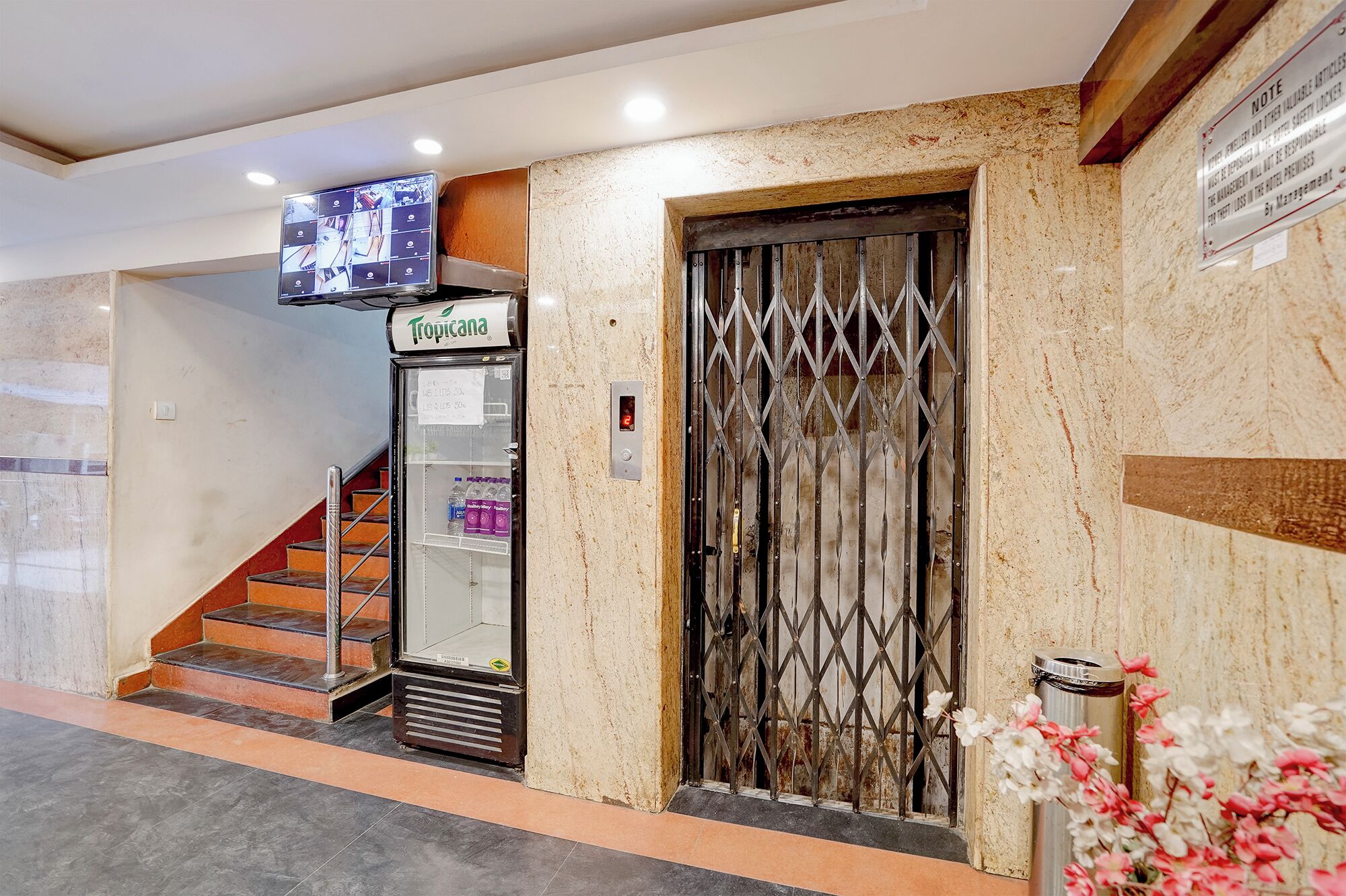 Un hall d’hôtel avec un escalier, un réfrigérateur de la marque Tropicana, une barrière de sécurité et une poubelle.