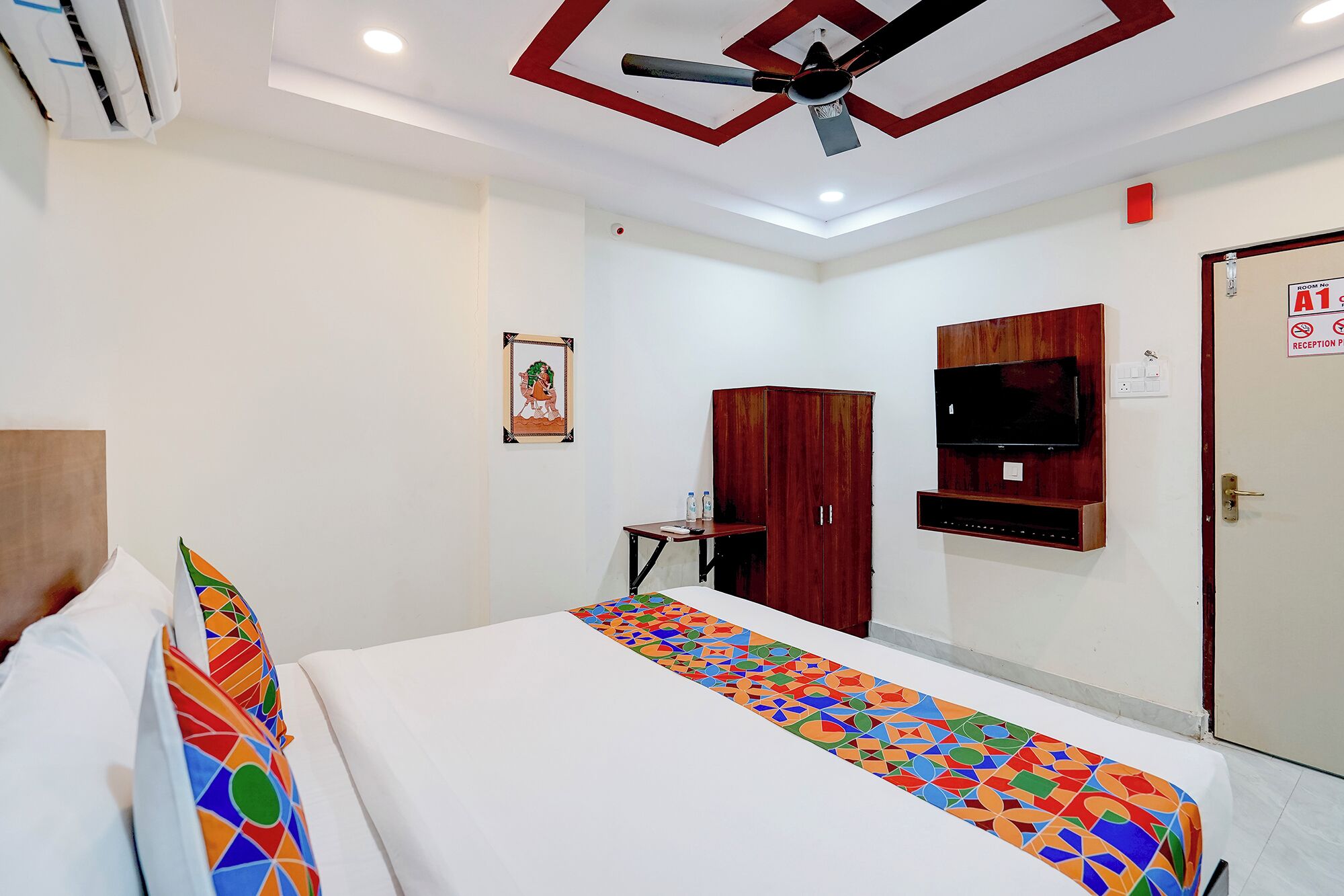Une chambre d’hôtel équipée d’un lit, d’un bureau, d’une armoire, d’une télévision et d’un ventilateur de plafond.