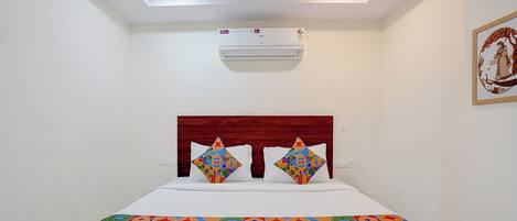 A hotel room with a bed, a ceiling light, an air conditioning unit, and a wall-mounted artwork.
