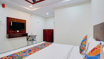 Une chambre d’hôtel avec un lit, un téléviseur fixé au mur, une armoire et une petite table avec une chaise.