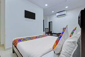 A hotel room with a bed, a flat-screen TV mounted on the wall, and an air conditioning unit.
