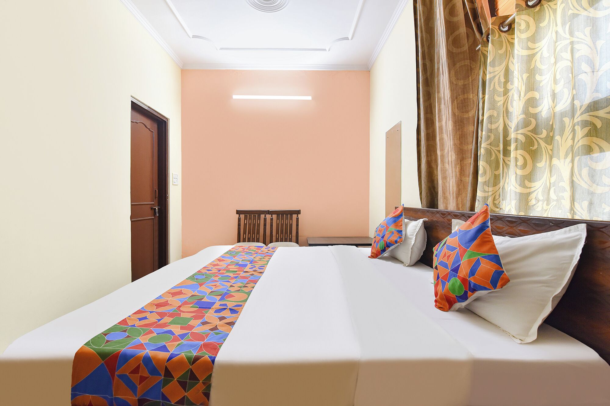 A hotel room with a bed, a bedside table, a chair, and a window with curtains.