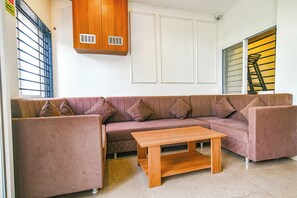 A living room with a brown sofa, a wooden coffee table, and a white wall with a window and a door.