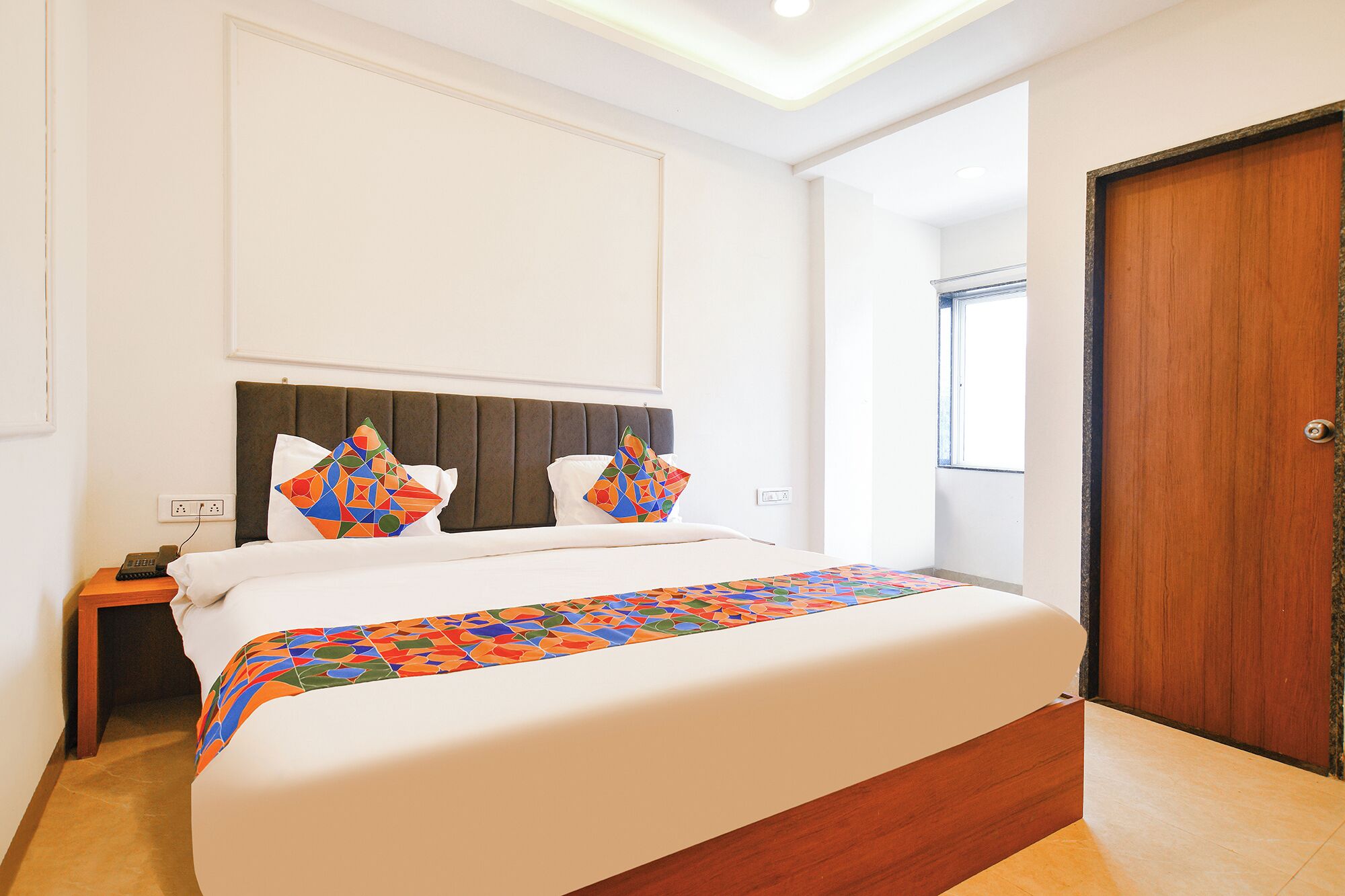 A hotel room with a bed, bedside table, and a wooden door.