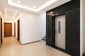 A modern hallway with a marble wall, a wooden door, and a digital elevator control panel.