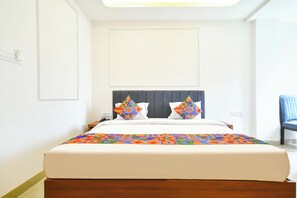 A hotel room with a bed, a bedside table, a chair, and a window. - FabHotel Tsj Grand (Indore)